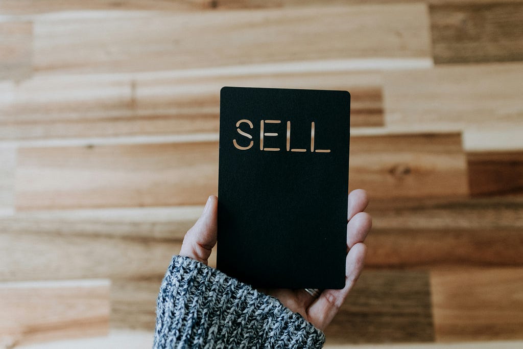 Person holding a black card that has the word “sell” on it