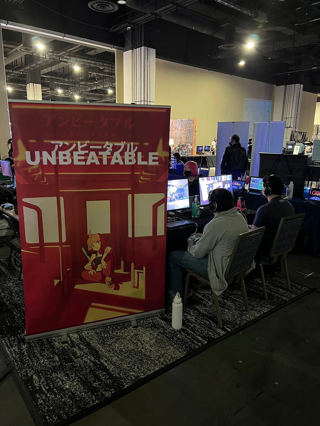 A picture of UNBEATABLE’s booth at MAGFest 2023, with a large poster and several demo setups shown.