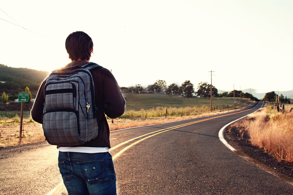 Image of a man with a backpack standing at the start of a long road.