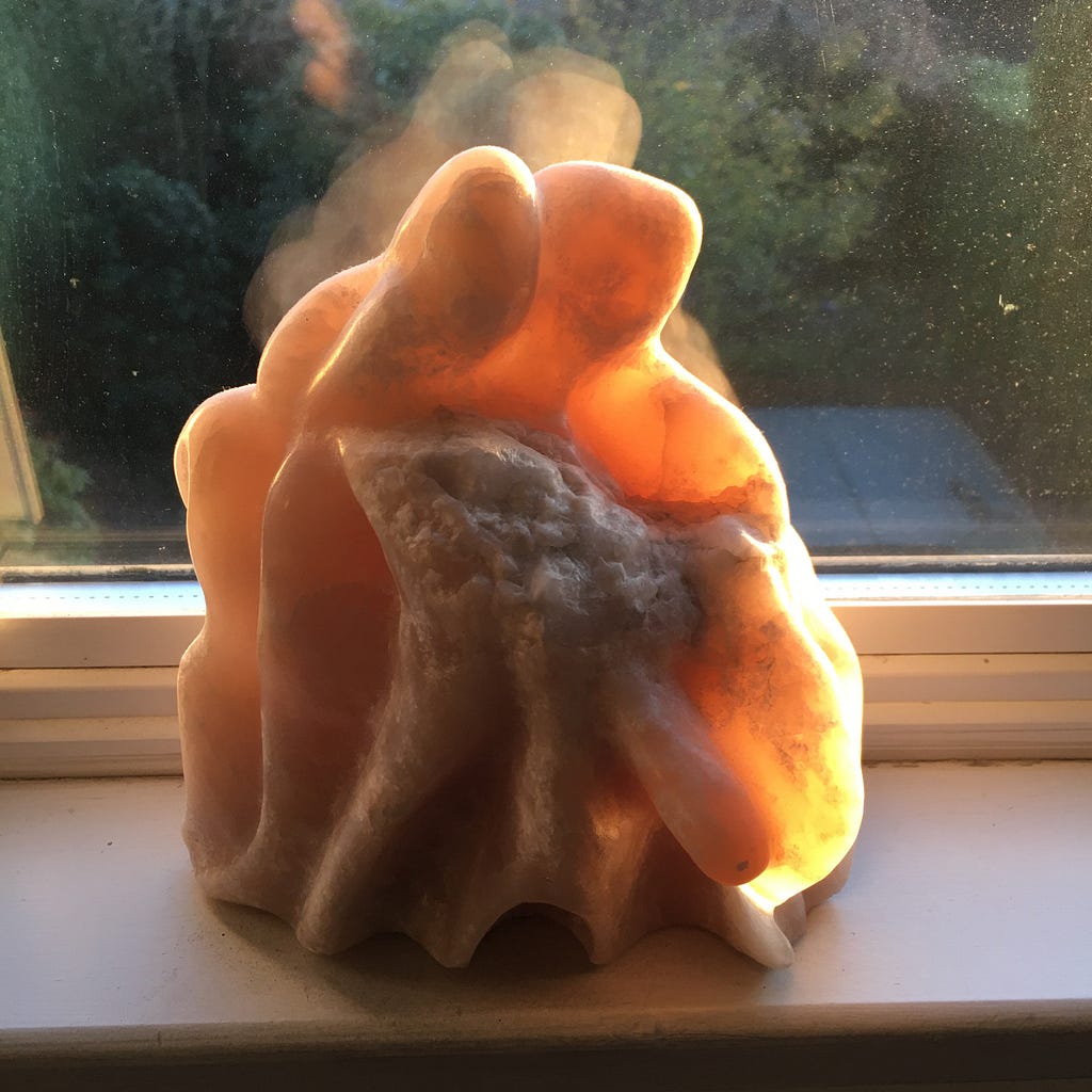 The sculpture has 2 faces translucently illuminated and beneath arms holding the child in shadowy rough stone. Veined Stone