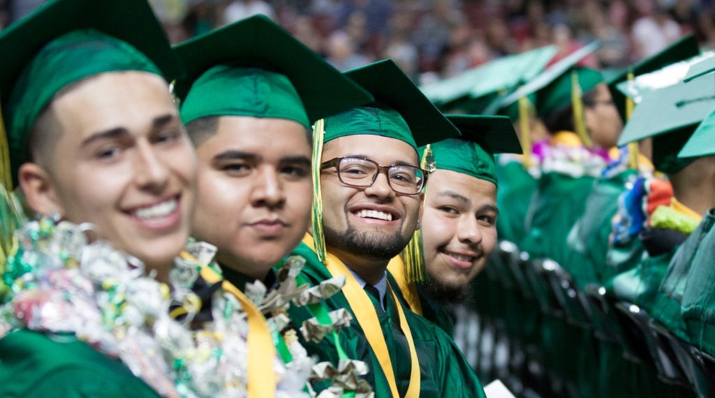 Four students smile in their green graduation caps and gowns