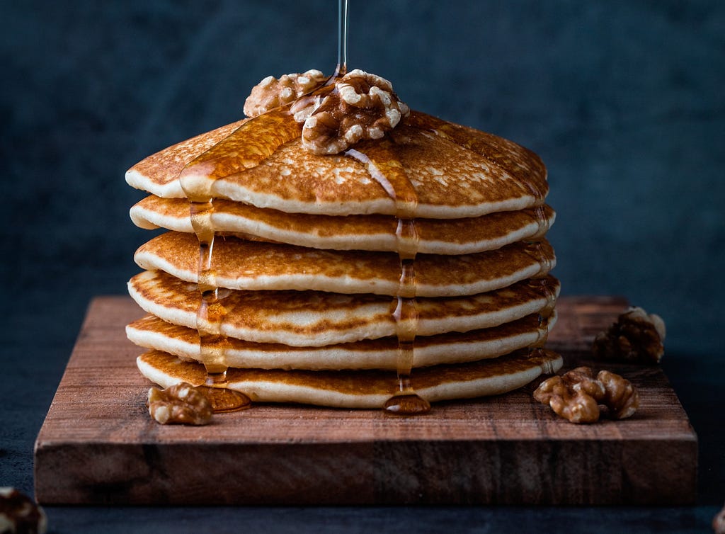 A stack of pancakes, garnished with syrup and walnuts