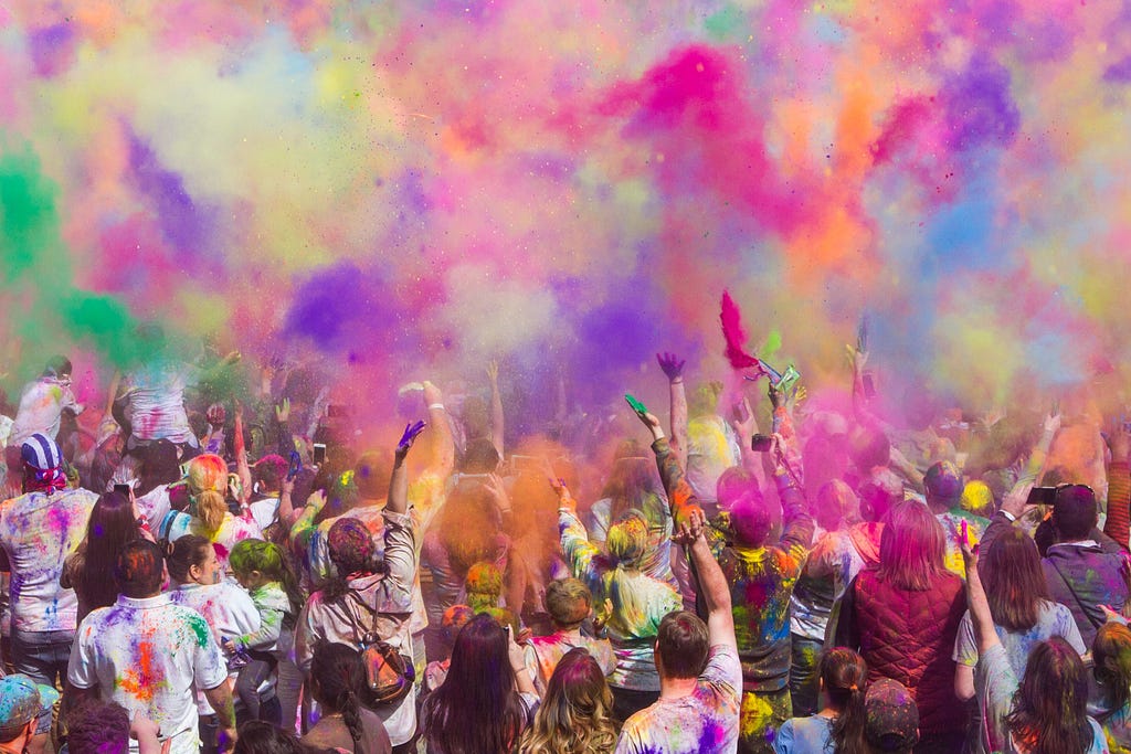 A large group of people with hands covered in paint lifted up to the colorful, painted sky.