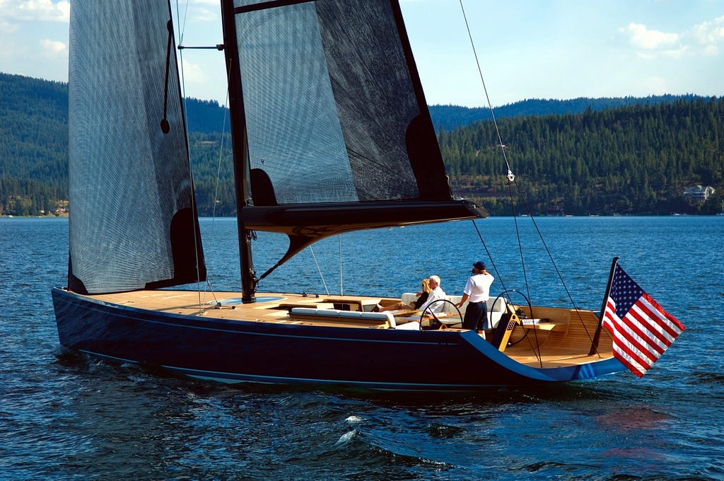An image showing the sleek design of a Daysailor sailboat, equipped with a set of pristine, white sails billowing in the wind against a backdrop of clear blue sky and calm waters.