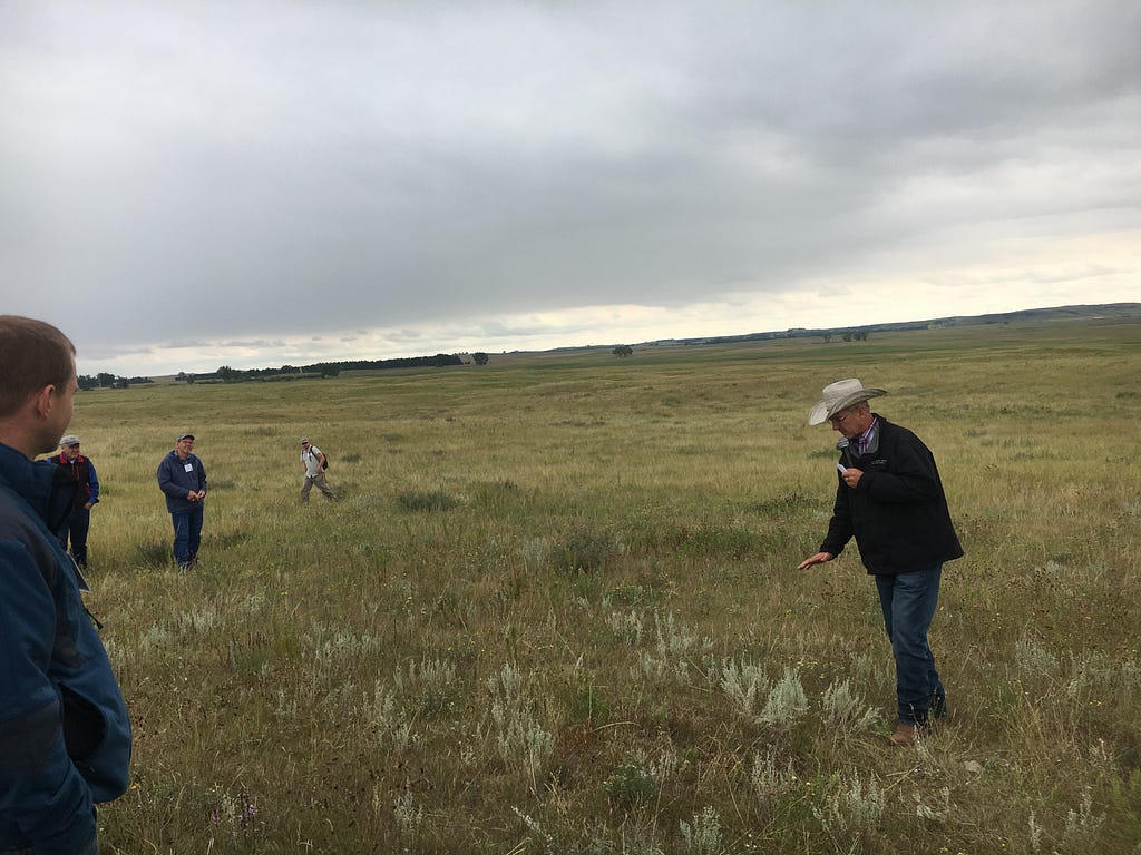 Jerry Doan, holding a microphone, gestures at the land as he speaks to a small crowd of people on his land