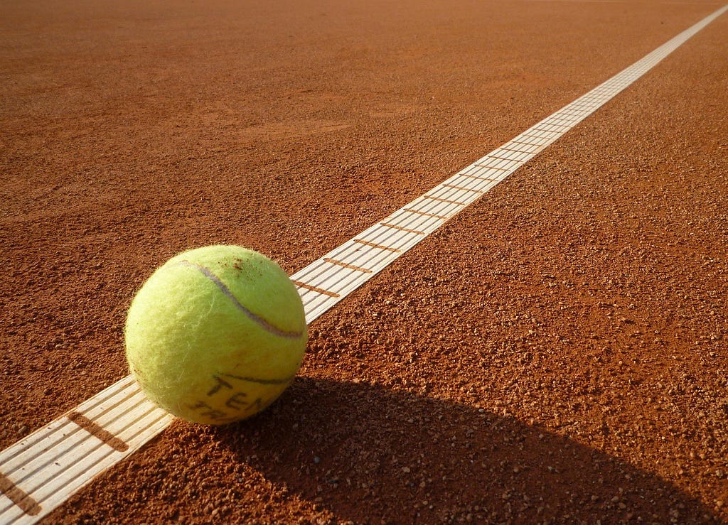 Image of a yellow tennis ball landing near the boundary line of a red clay court