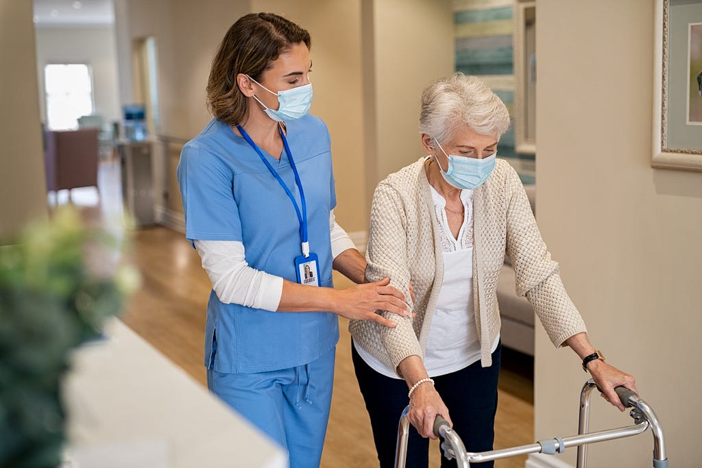 A nurse helping an elderly lady down a hallway with a walker.