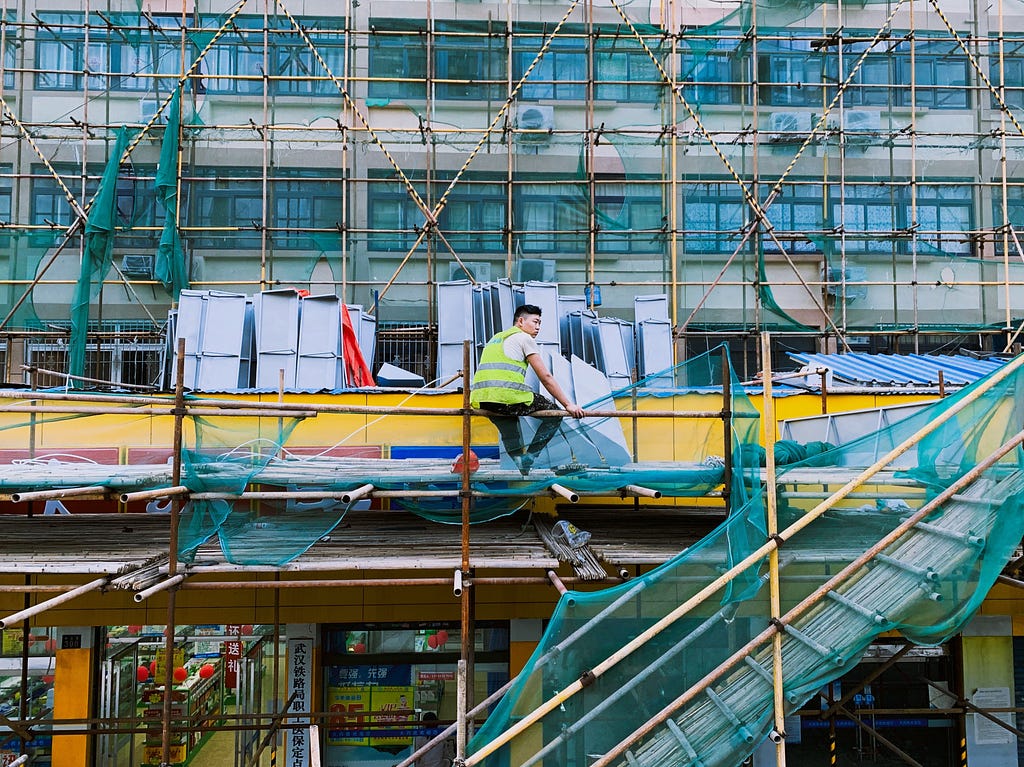 A man in a hi-vis vest sits alone on scaffold.