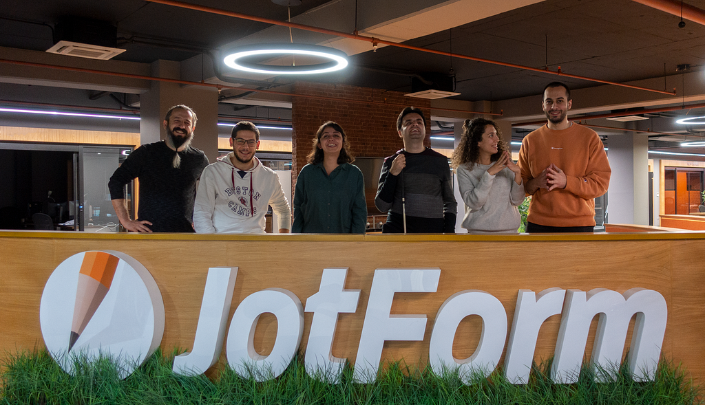 A photo of five user researchers and Cagrı over a JotForm logo at the entrance of JotForm Ankara office.