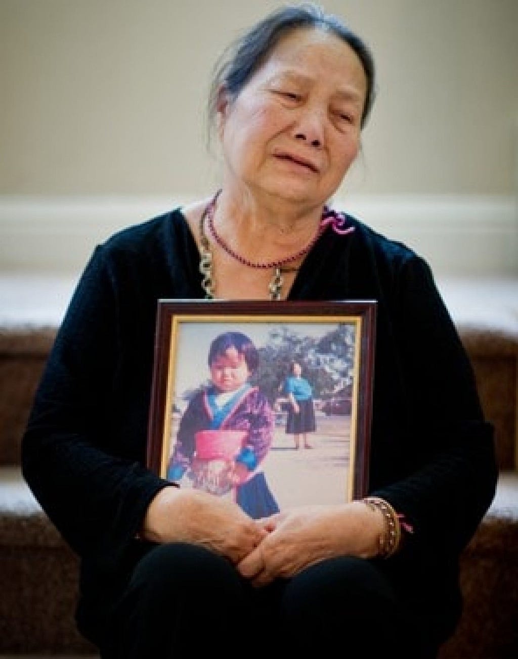 Image of Foua, mother to Lia Lee, holding a portrait of Lia at their funeral procession.