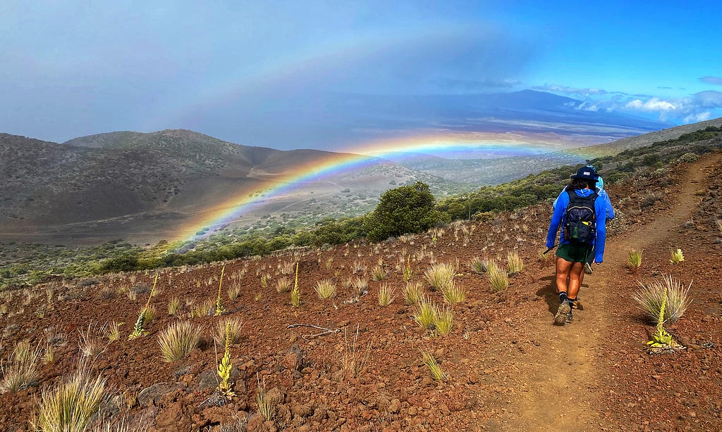 Hikers approach a rainbow on a Hawaiian volcano.