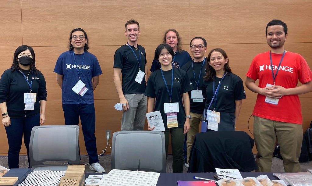 A group pic of HENNGE employees at the conference. Many are wearing a sports tee with a small HENNGE logo over the heart.