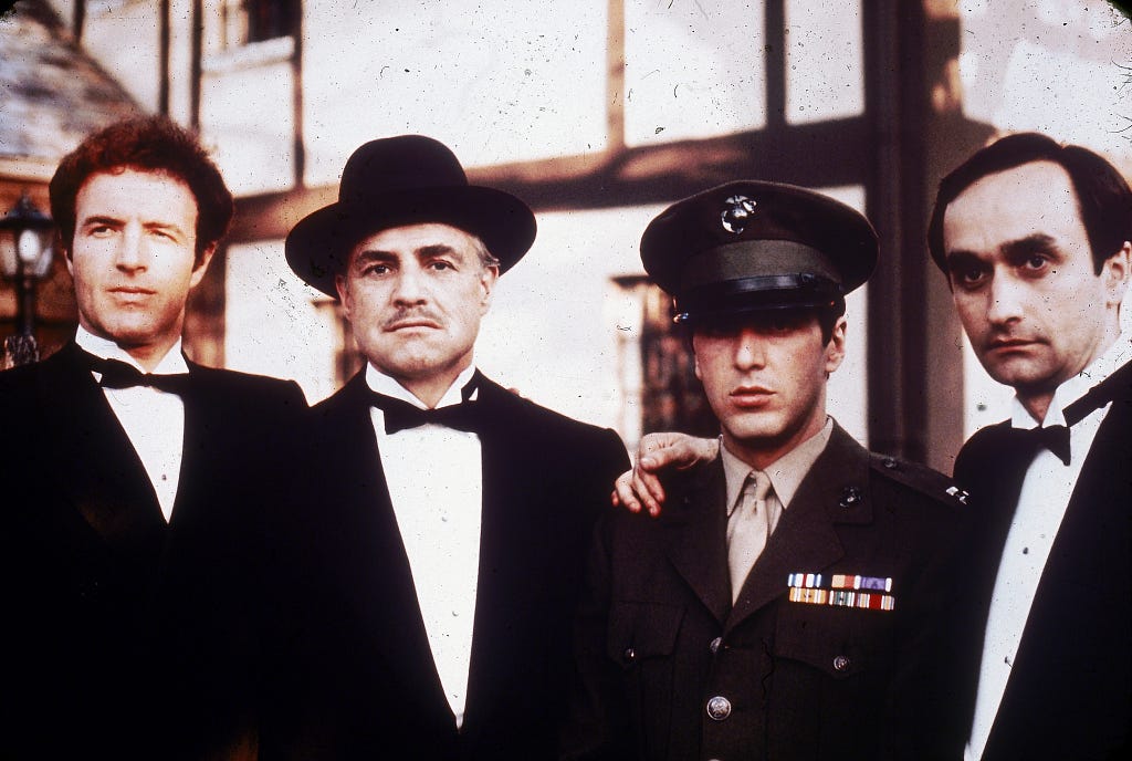 Three men in black tie standing with a fourth, dressed in military gear with medals hanging from his chest.