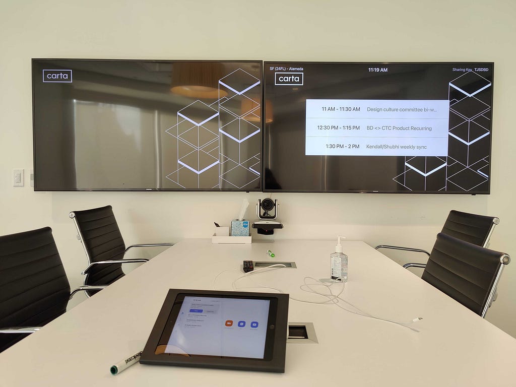 a meeting room with a table, chair, and tvs