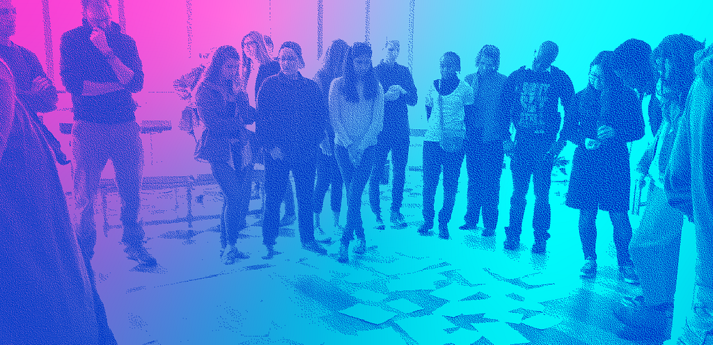 Another psychedelic-style color treatment on this image, with light blue and hot pink. A group of about 13 students stand in a wide circle around papers arranged on the floor, at their feet.