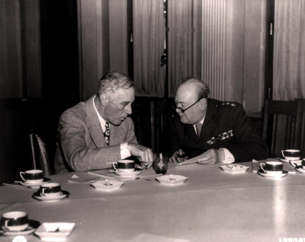 Photo shows President Franklin D. Roosevelt and Prime Minister Winston Churchill sitting and talking at a conference table with coffee cups in front of them at the Yalta Conference 1945.