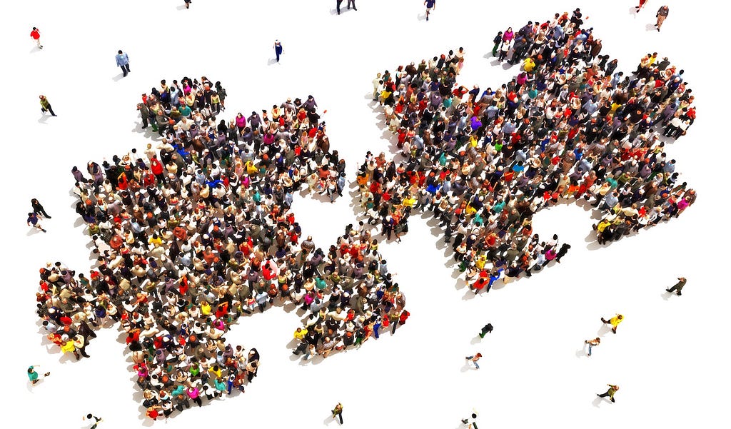 Many diverse people grouped together to form two puzzle pieces about to connect.