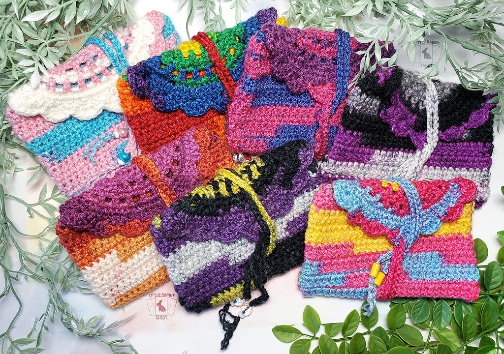 A photo of a colorful crochet bags, sized perfectly for a standard tarot deck. All various pride themed colors.