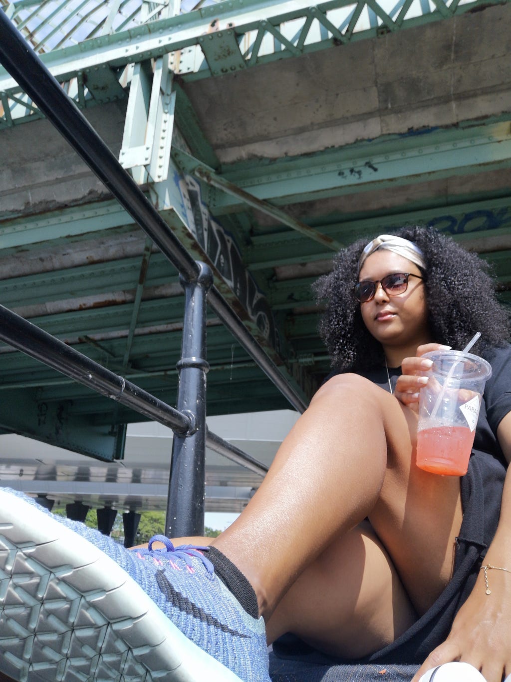 Photo by Samah Fadil | Girl sits underneath a bridge holding to-go cup