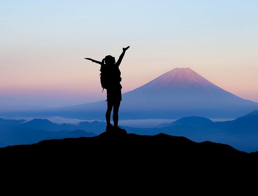 person standing at the top of a mountain while the sun comes up