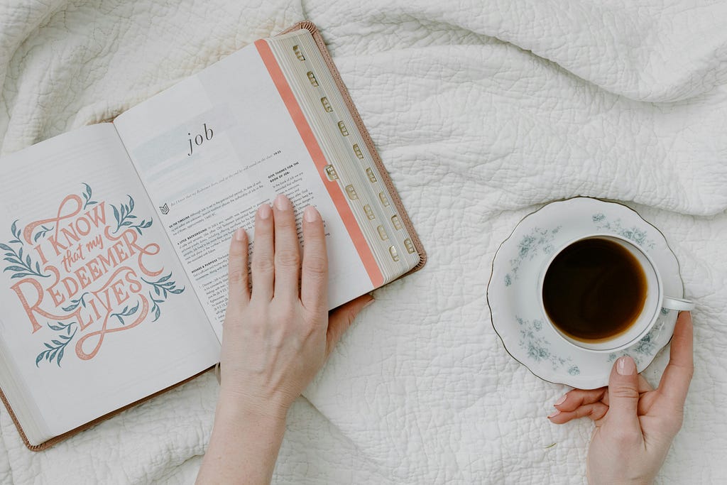 An open Bible and cup of coffee on the bedsheet.