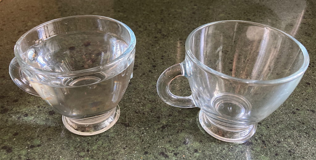 Two cups, one filled with water and the other empty