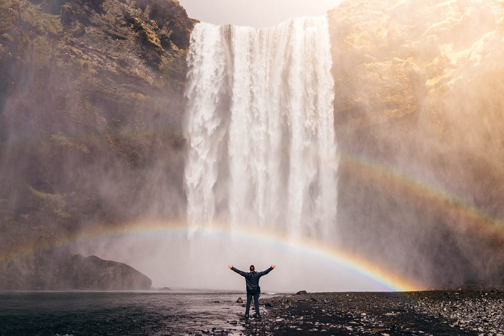 Person standing in awe of a large, beautiful waterfall.