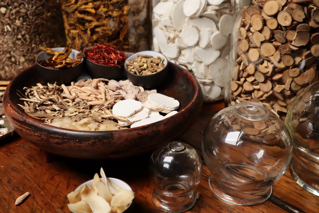 A wide variety of Traditional Chinese Medicine on a table in a splash of colours: red, light brown and dark brown, white, and yellow.