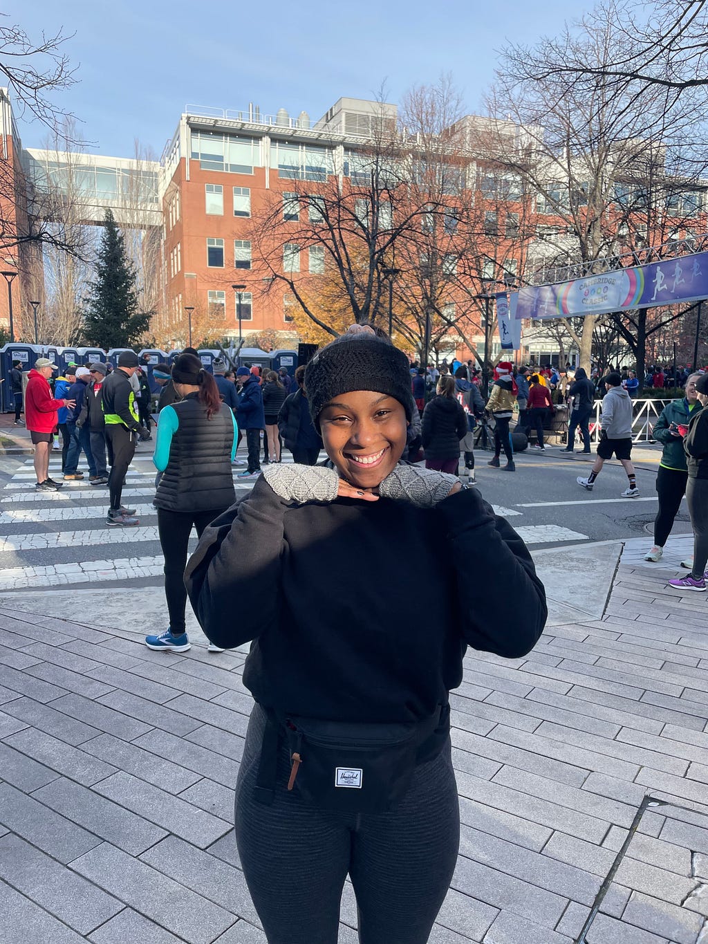 Natalie Cantave posing in front of a running start line with a black headband, black sweatshirt, and grey gloves