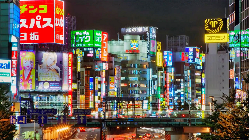 A Japanese city landscape is illuminated by bright billboards at night