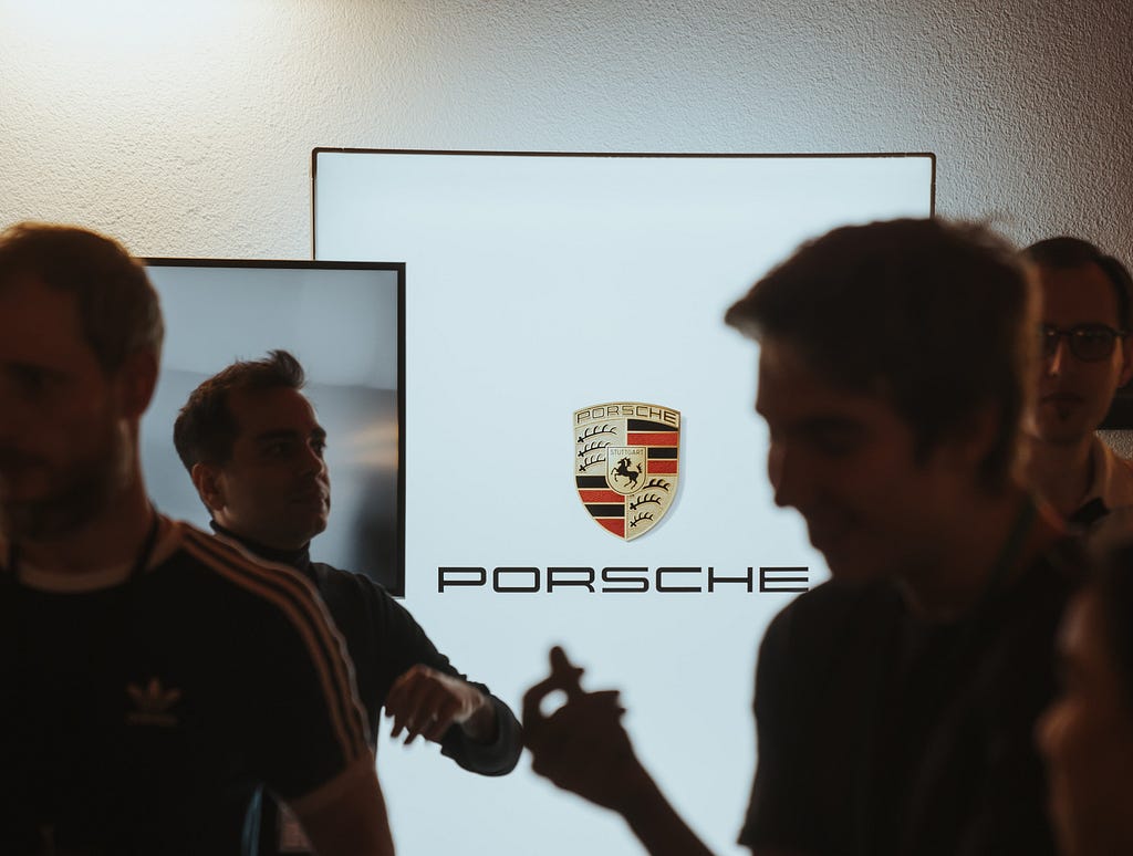 The Porsche logo on a digital screen with people in front of it.
