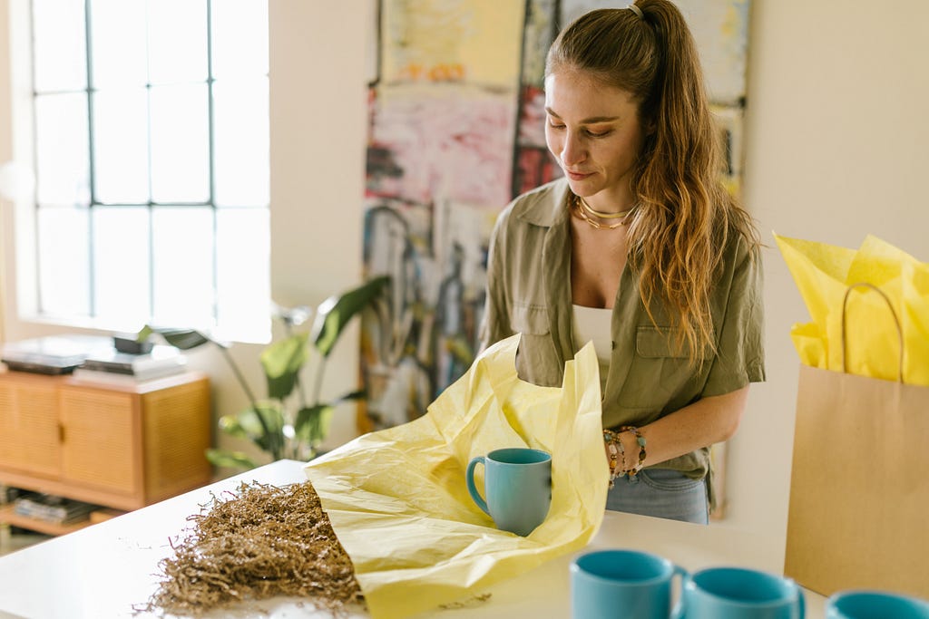 Woman wrapping blue mugs in tissue paper