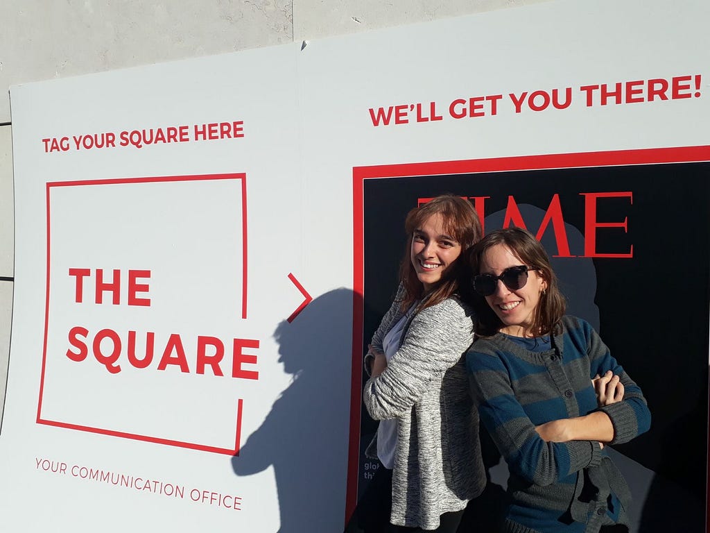 Two females standing close to each other smiling for the camera, next to a frame