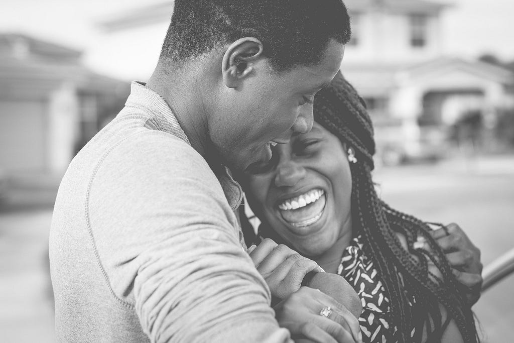 A happy black couple holding and hugging each other, heartily laughing/smiling