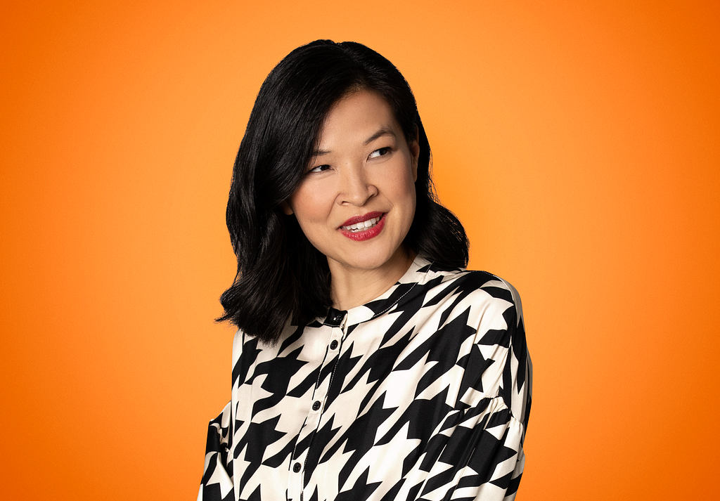 A photo of journalist, author and podcaster SuChin Pak with an orange background