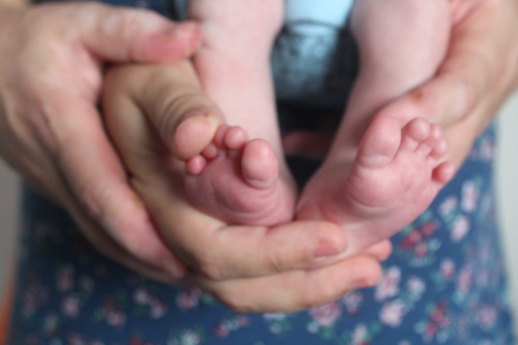 Mãos do pai e da mãe segurando os pés de um recém nascido