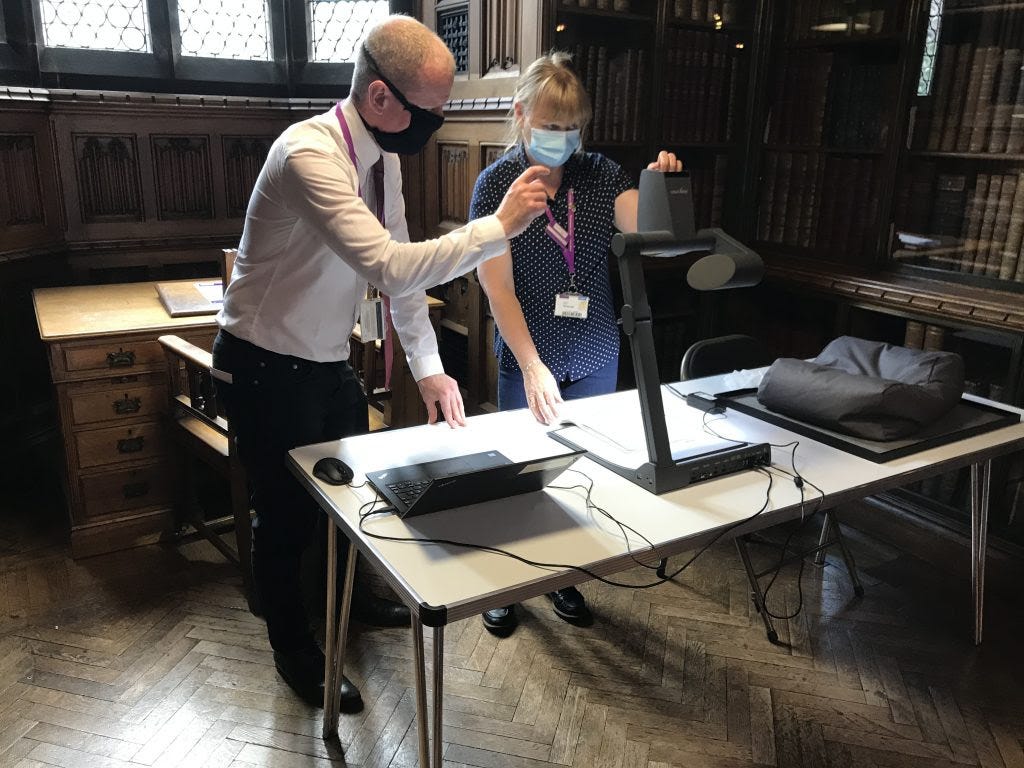 Two staff members standing behind a desk, on which is a laptop and a visualiser.