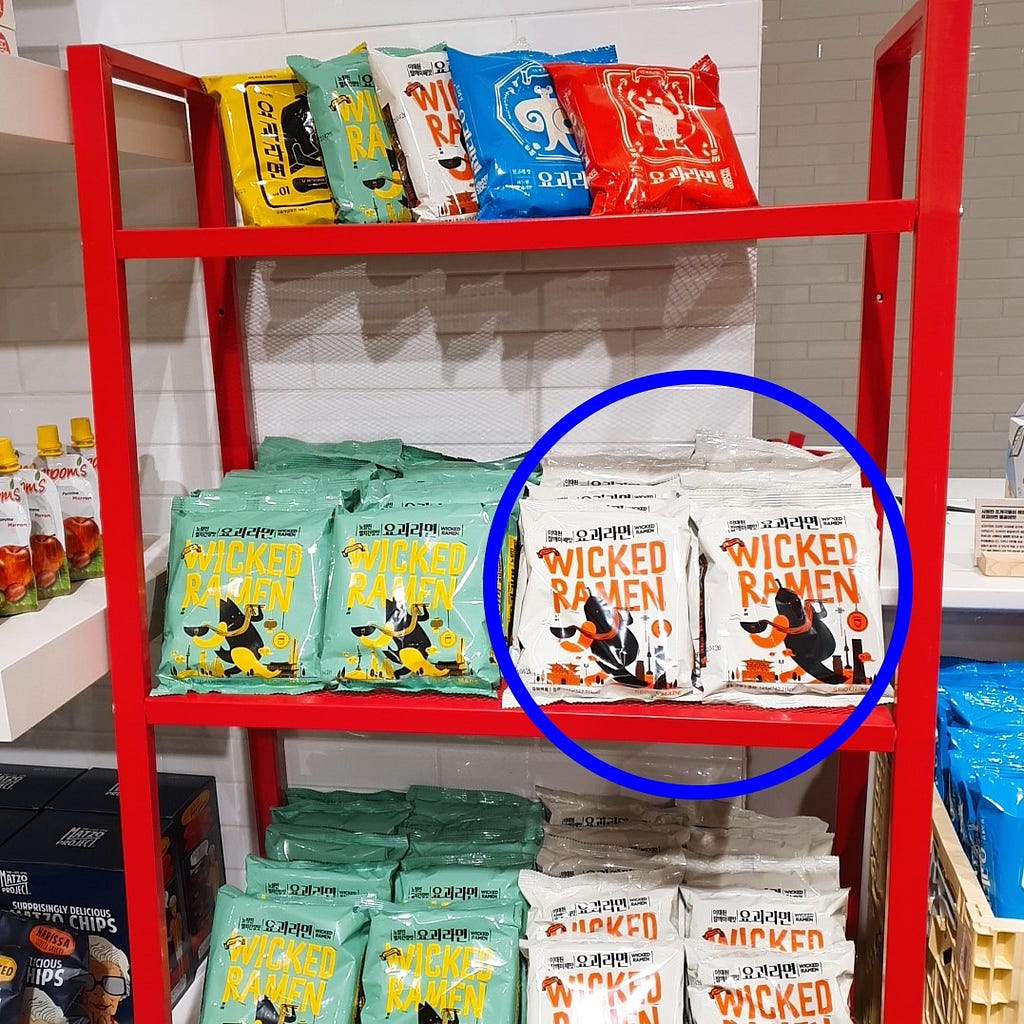 A blue circle pointing out the Wicked Ramen (Yogoe Ramyeon) Itaeweon Chamggae Majemat packages on a shelf.
