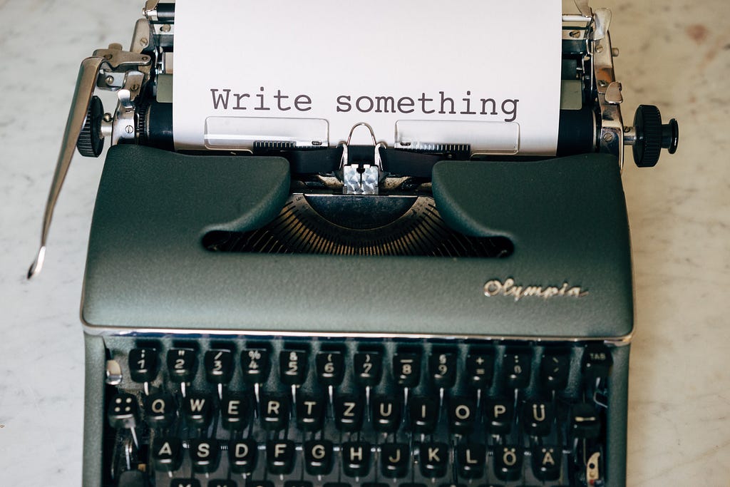An antique typewriter with a piece of paper reading, “Write something.”