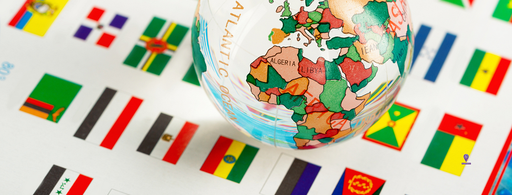 Glass globe with image of African countries outlined sitting on a white sheet imprinted with flags from various countries.