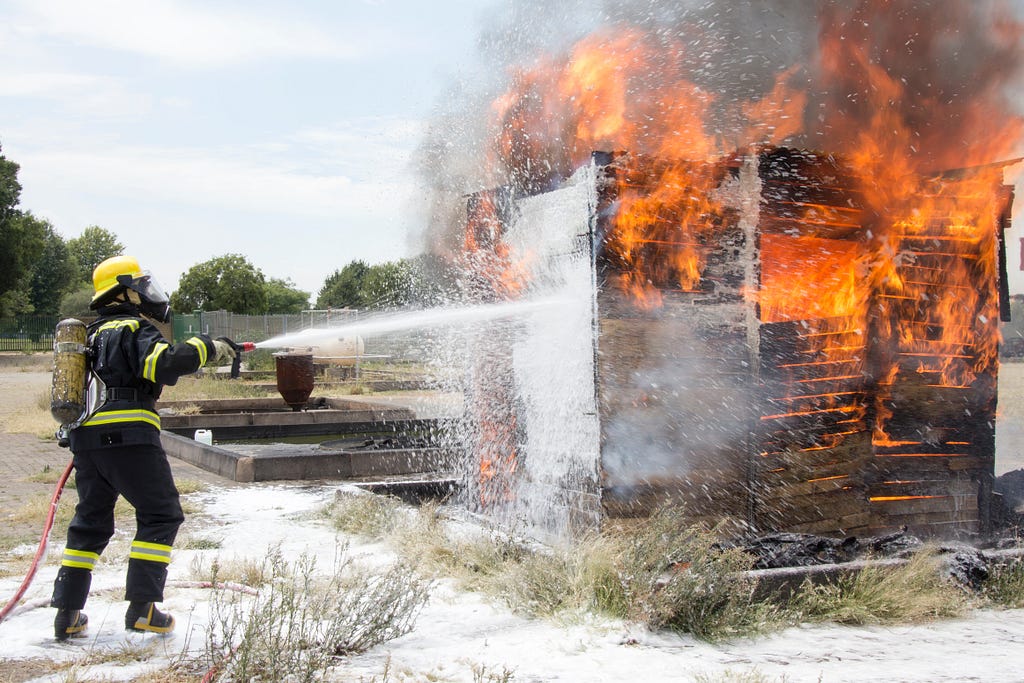A fireman putting out a practice fire made of wood with a foam spray.