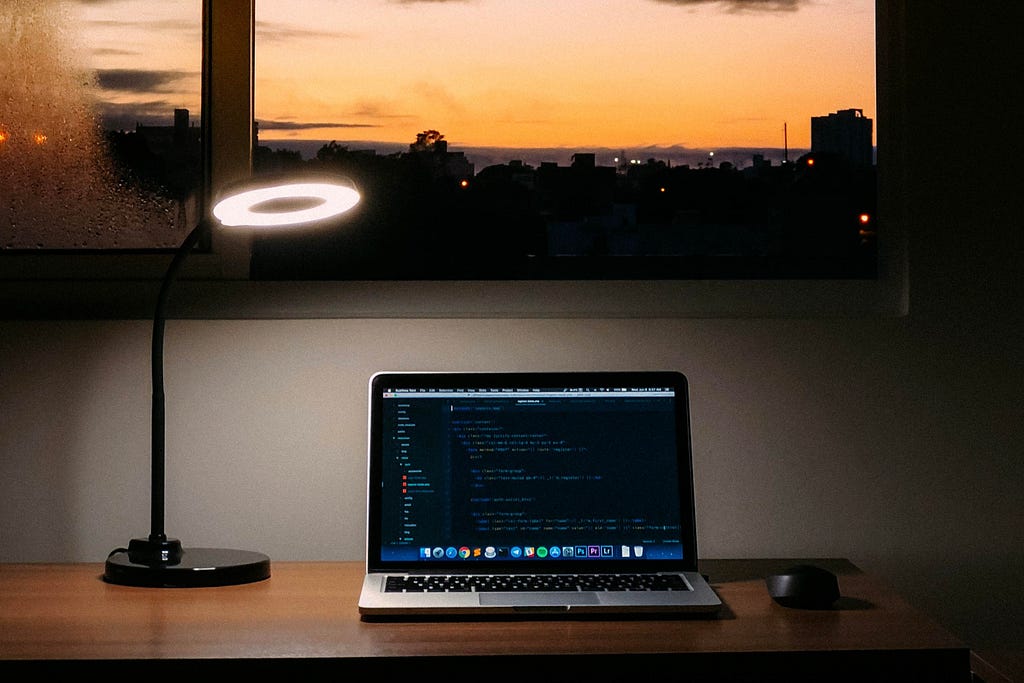 A macbook sitting on a desk in a dark room, overlooking a twilit sky.