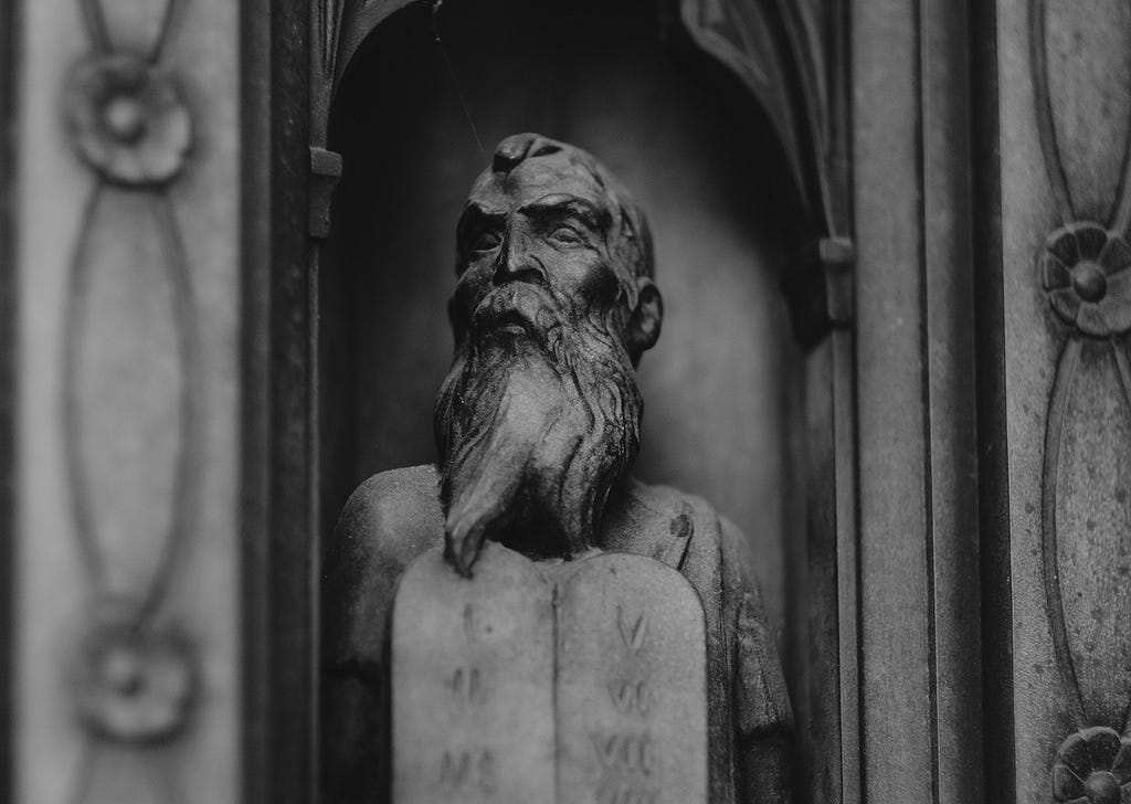 Grey concrete statue of Moses holding the tablets of the Ten Commandments, from a door at Forest Lawn Memorial Park.