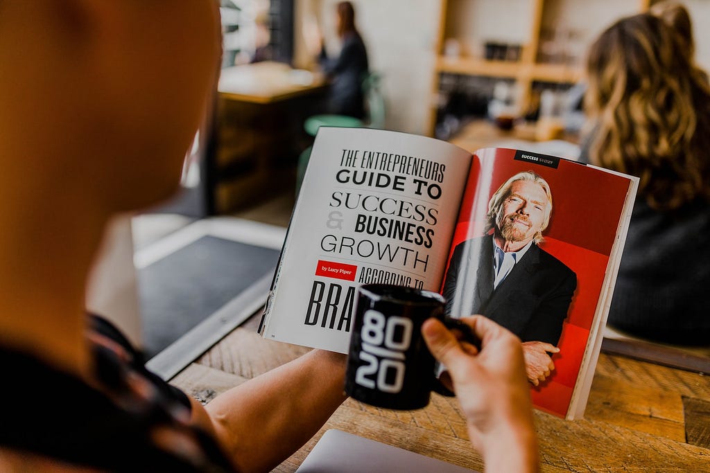 A photo that shows someone reading a book that features Sir Richard Branson, while holding a mug.