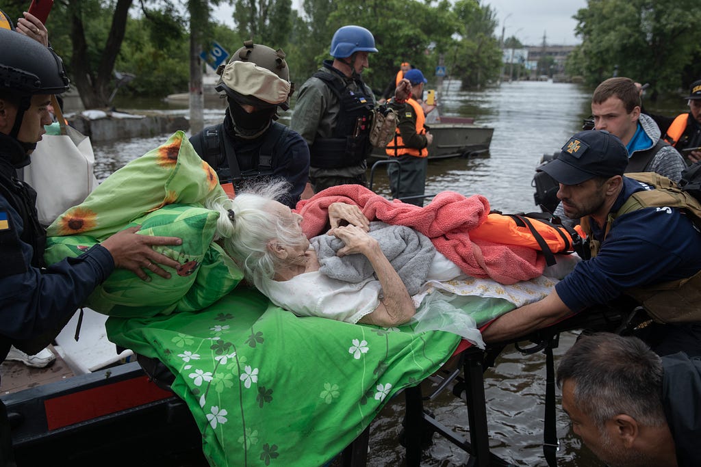 Rescuers in knee-deep waters work to evacuate a woman laying on a stretcher wrapped in several blankets.