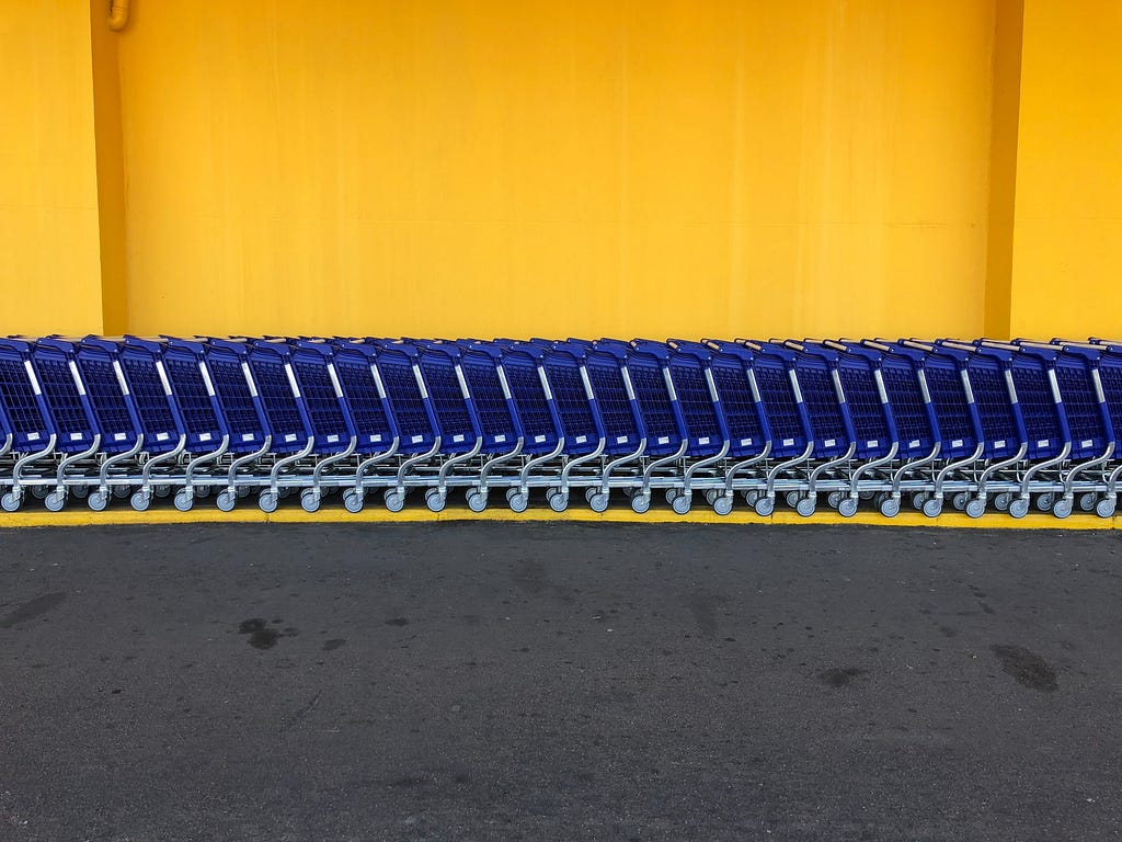 A row of blue shopping carts in front of a yellow wall.