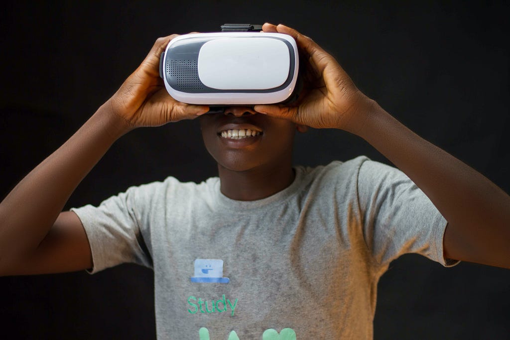 A child is using Virtual Reality goggles and is smiling while holding them over his eyes