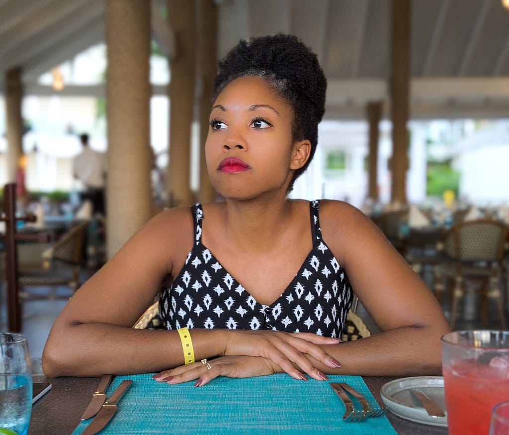 Black woman sitting at an empty dining space staring thoughtfully into the distance.