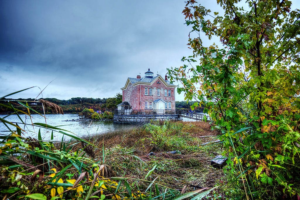 two story red brick lighthouse on a river