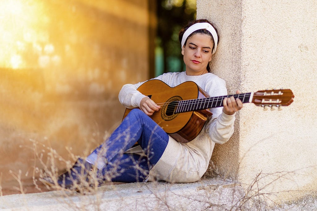 A woman sitting alone outside and playing the guitar